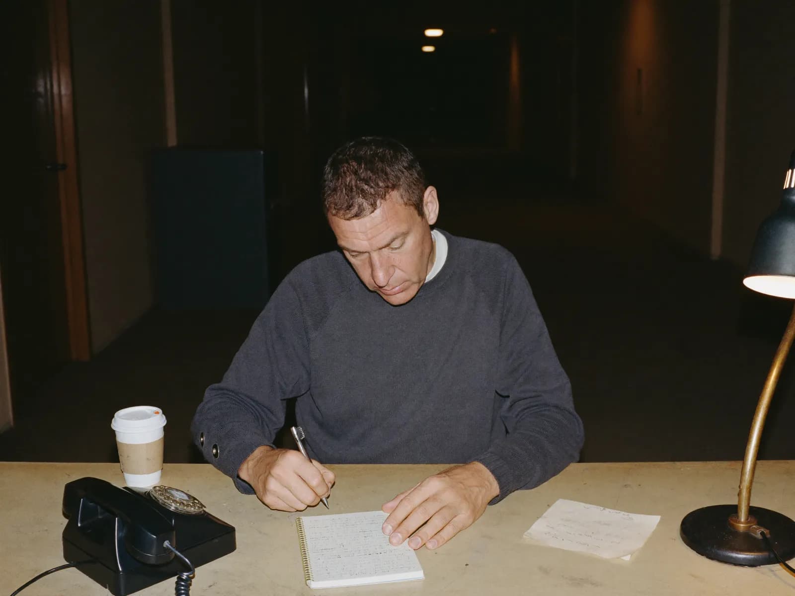 Night-shift worker writing a paper logbook entry at a building reception desk