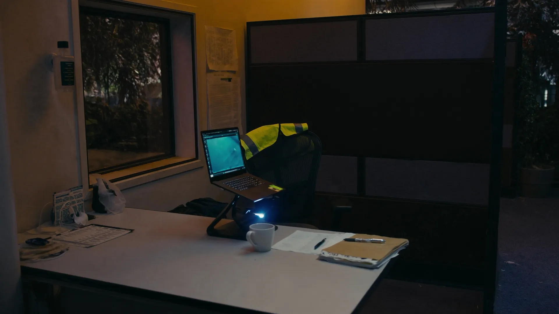 A small founder-run workspace with a laptop and a hi-vis vest on the chair